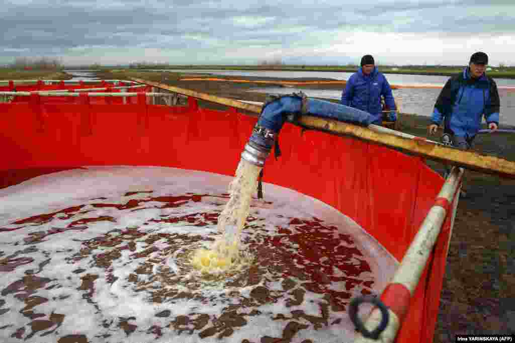 Workers fill a collection tank with a mixture of oil and water skimmed from the surface of the contaminated Ambarnaya River.