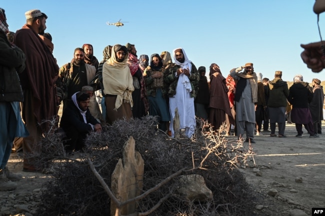 Afghan men gather around the grave of Khalil Ur-Rahman Haqqani, the Taliban refugees and repatriation minister. The Islamic State group claimed his assassination in December.