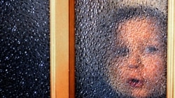Воспитанник детского дома смотрит через стеклянную дверь. Иллюстративное фото.