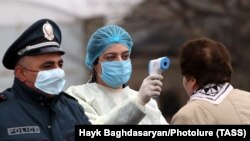 An Armenian medical worker measures the temperature of a woman at an entrance to the city of Vagharshapat as part of the country’s measures taken to prevent the spread of the coronavirus