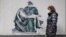 A woman walks past a mural depicting a medical worker in a pose like that of Michelangelo's famous Pieta sculpture, on a wall near a vaccination center in the Bulgarian capital, Sofia.