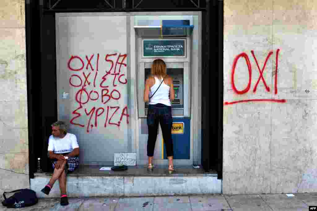 A woman withdraws money from an ATM machine next to a beggar and graffiti reading "No To Fear" in Thessaloniki, Greece. (AFP/Sakis Mitrolidis)