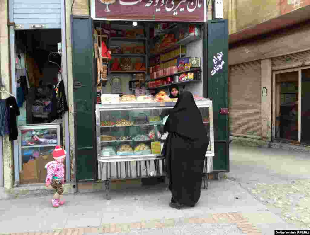 Старушка в чадоре покупает сладости для своей внучки на улице в Ширазе. Молодые женщины предпочитают вместо чадора носить манто&nbsp;​&ndash; приталенную курточку