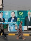People walk past electoral campaign posters ahead of Iraq's parliamentary elections in central Baghdad on November 6.