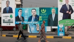 People walk past electoral campaign posters ahead of Iraq's parliamentary elections in central Baghdad on November 6.