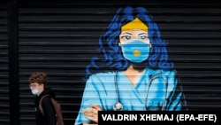 Мальчик в защитной маске идет рядом с фреской с изображением медсестры на фоне продолжающейся пандемии коронавируса COVID-19 в Приштине, Косово, 3 декабря 2020 года