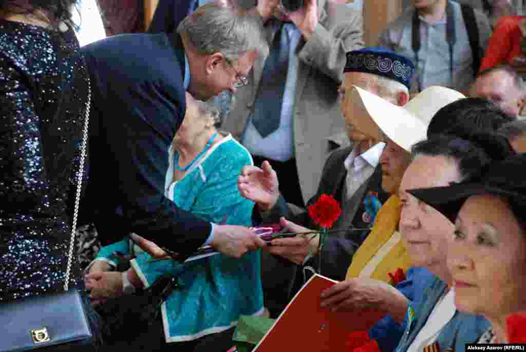 Пососл США в Казахстане Джордж А. Крол поздравляет каждого пришедшего на фотовыставку ветерана фронта и тыла, вручая по красной гвоздике.