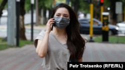 Девушка в защитной маске идет по улице Алматы. 22 июня 2020 года.