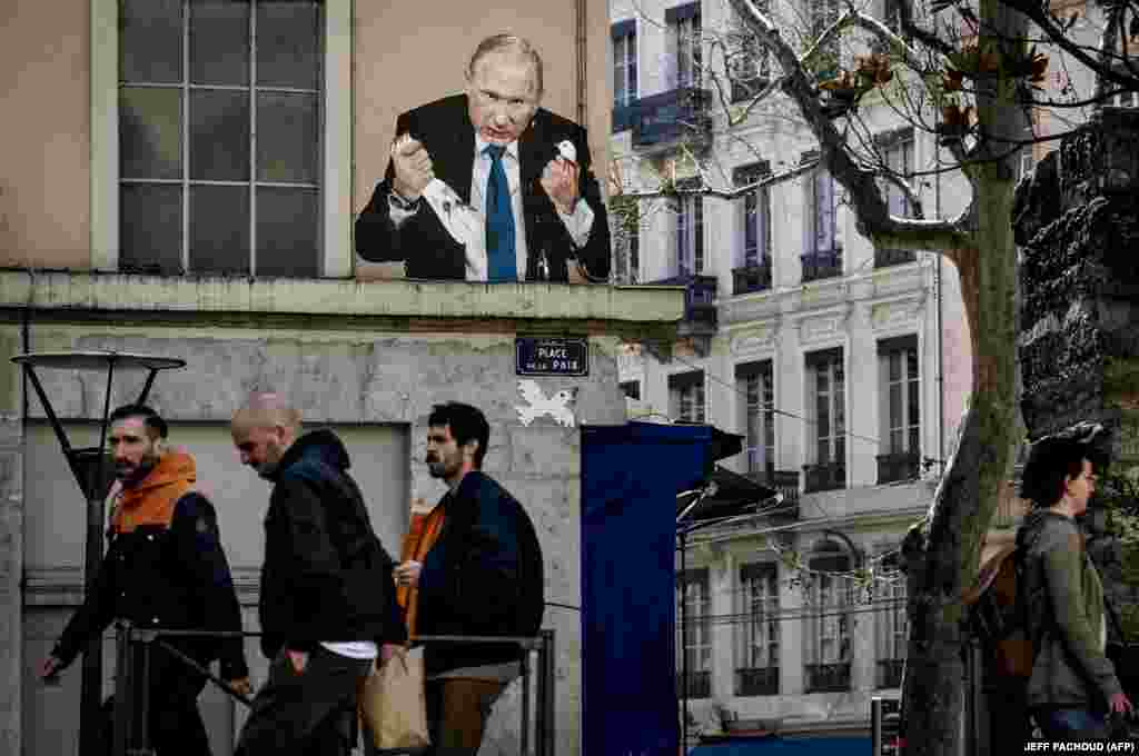 Oamenii trec pe lângă o pictură murală care îl înfățișează pe Putin smulgând capul unui porumbel, în Place de la Paix din Lyon, Franța, pe 22 martie, de către un artist necunoscut.