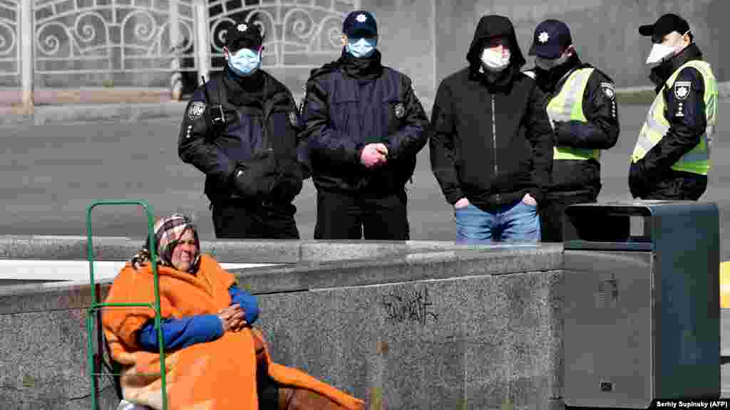 Маска таққан полиция қызметкерлерінен қайыр садақа сұраған баспанасыз әйел. Киев, Украина.
