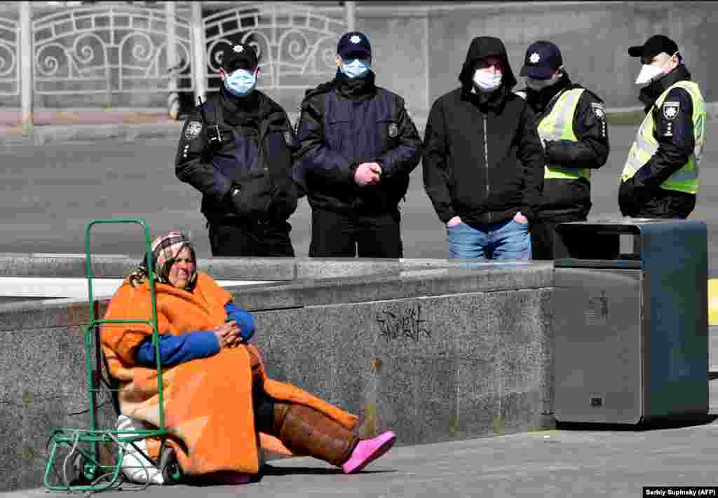 An elderly homeless woman begs in Kyiv, Ukraine, as police wearing face masks patrol the streets amid a coronavirus outbreak. (AFP/Sergei Supinsky)