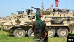Un membru al Unităților de Kurde de Apărare a Poporului și mai multe vehicule blindate americane la granița dintre Turcia și Siria, 29 aprilie 2017
