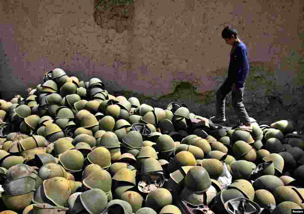 An Afghan boy walks by a pile of Russian-made helmets in the Panjshir Valley in August 2005.
