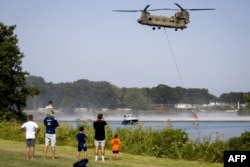 Trecătorii privesc cum un elicopter CH-47 Chinook al Forțelor Aeriene Regale Olandeze ia apă din râul Meuse, în Geijsteren, pentru a combate un incendiu de pădure.