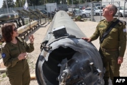 Purtătorul de cuvânt al armatei israeliene, amiralul în retragere, Daniel Hagari (dreapta), și adjuncta sa, Masha Michelson, pozează cu o rachetă iraniană căzută în Israel, la Kiryat Malachi, trei zile după atacul din 13 aprilie.