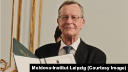 Klaus Bochmann, președintele Institutului Moldova Leipzig, la evenimentul de aniversare a 20 de ani de la fondarea organizației, cu o diplomă de excelență din partea Universității de Stat din Moldova, Chișinău, februarie 2026