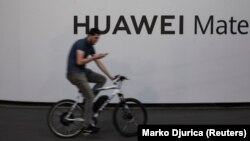 Huawei компаниясының көшедегі жарнамасының тұсынан өтіп бара жатқан велосипед мінген адам. Белград, Сербия, 12 тамыз 2020 жыл.
