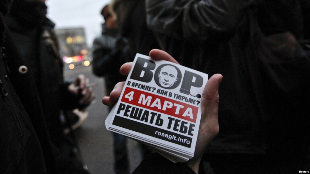 An activist shows a sticker with an image of Prime Minister Vladimir Putin that says: "Thief in the Kremlin? Or in prison? March 4, you decide."