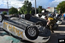 A protester ties his shoelaces on an overturned car.