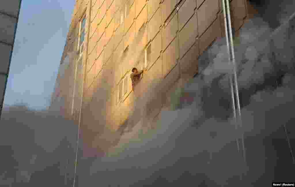 A survivor dangles from a windowsill as he waits for rescue from a burning building in Jecheon, South Korea, on December 21. (Reuters)