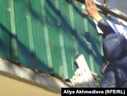 Молодой человек забрался по приставной лестнице к балкону квартиры жительницы поселка Карабулак Зои Юртаевой и срывает плакаты со словами протеста. Алматинская область, 18 декабря 2015 года.