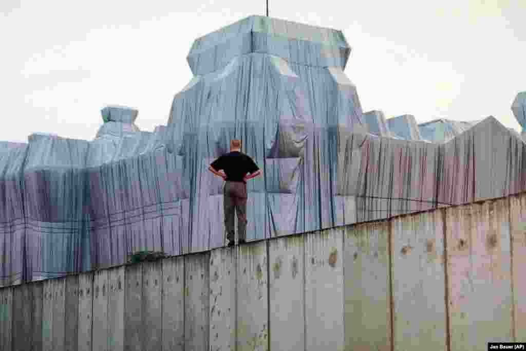 A man stands atop the remains of the Berlin Wall and looks at the wrapped Reichstag building in June 1995.