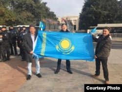 Участники акции протеста в Женеве Кыдырали Оразулы, Омирхан Алтын и Аманжан Сейит (справа налево) держат казахстанский флаг. 6 ноября 2018 года