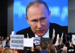 A video screen shows Putin speaking during his annual press conference last year while journalists hold up signs showing their media affiliations.