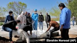 People wearing protective clothing, masks and gloves, attend the funeral of a victim who died of new coronavirus, at a cemetery just outside Tehran, March 30, 2020