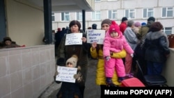 Local residents hold signs, with one reading "Don't kill our kids!" as they gather outside the hospital in Volokolamsk on March 21.