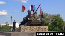 Tineri pozând pe tancul din centrul Tiraspolului, cu drapele ale Transnistriei, Rusiei și URSS.