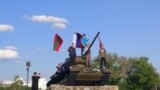 Tineri pozând de Ziua Victoriei pe tancul din centrul Tiraspolului, cu drapele ale Transnistriei, Rusiei și URSS