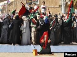 Женщина на одной из площадей Триполи молится за умерших, в то время как толпа празднует смерть Муаммара Каддафи. 21 октября 2011 года