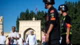 Китайские полицейские наблюдают за уйгурами, выходящими после молитвы из мечети Ид Ках в городе Кашгар. 2019 г.