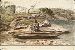 A native woman sits by a canoe, probably in Australia.