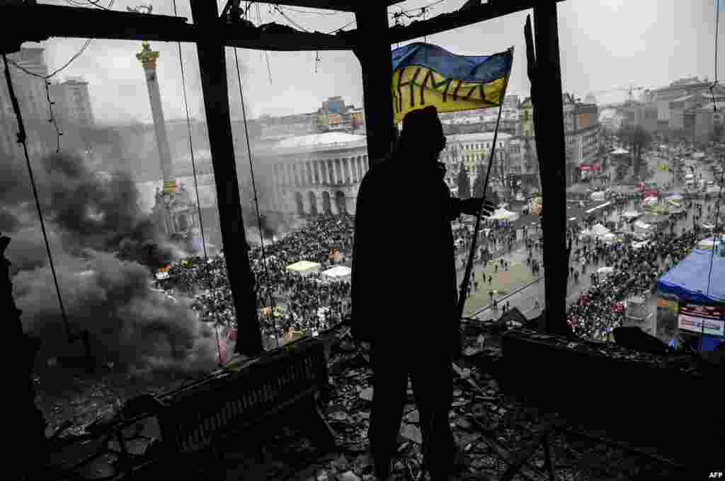 A protester holds a Ukranian national flag from a burned building.