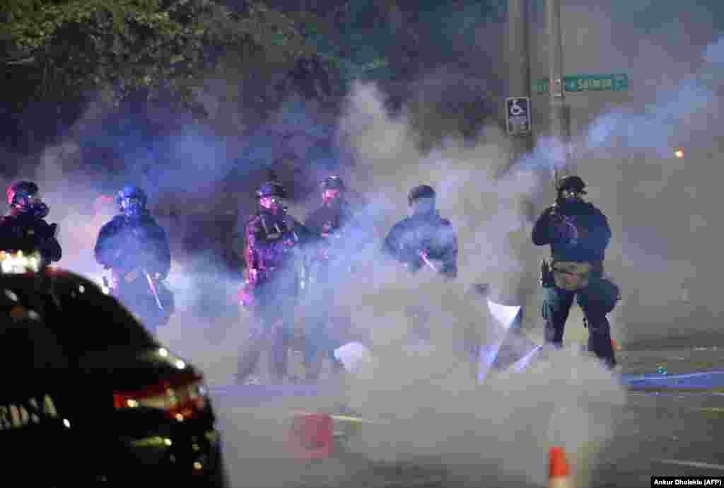 Security personnel stand in a cloud of tear gas in Portland, Oregon early July 26, 2020, as protests continue across the United States following the death in Minneapolis of unarmed African-American George Floyd. - Police and federal agents fired tear gas and forcefully dispersed protesters in the US city of Portland, amid President Donald Trump&#39;s heavily-criticized &quot;surge&quot; of security forces to major cities. The city, the biggest in the state of Oregon, has seen nightly protests against racism and police brutality for nearly two months, initially sparked by the death of unarmed African American George Floyd at the hands of police in Minnesota (Photo by Ankur Dholakia / AFP)