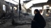 A woman sits outside her burnt-out house after the violence on February 7- 8.