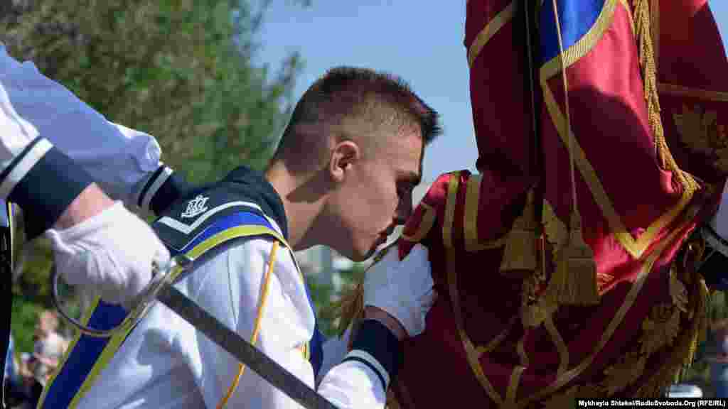 Старий&nbsp;прапороносець цілує прапор на прощання і передає його молодому, який також торкається губами знамені