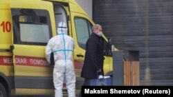 Мужчина в защитной маске проходит мимо машины скорой помощи и больницы для пациентов с коронавирусом на окраине Москвы. 20 апреля 2020 года.