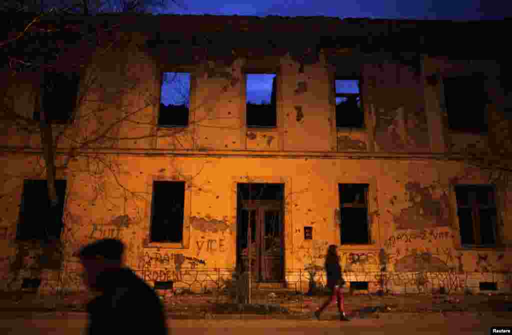 People walk by an abandoned building. Mostar remains divided along ethnic lines, with Croat and Bosniak schoolchildren attending separate classes and studying from separate textbooks.