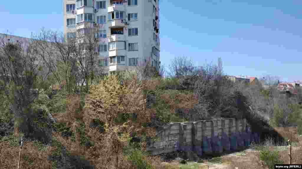 Над оврагом нависает девятиэтажка-свечка с улицы Кокчетавской, склон держит мощная подпорная стена