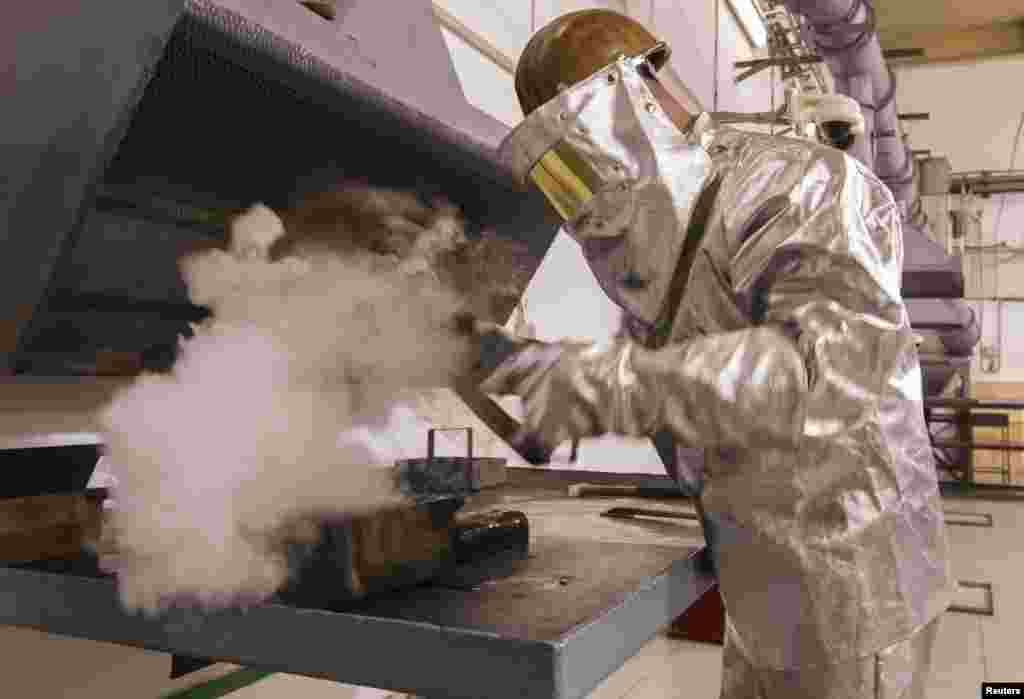 A worker wearing heatproof suit takes a gold alloy bar out of mould in a workshop of Altyntau gold mine extraction factory.