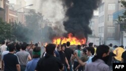 Supporters of Iran's presidential candidate Mir Hossein Mousavi standing by a burning vehicle during protests in Tehran, 19Jun2009