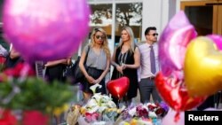 People look upon the flowers, messages, and tokens left in tribute to the victims of the attack on Manchester Arena. 