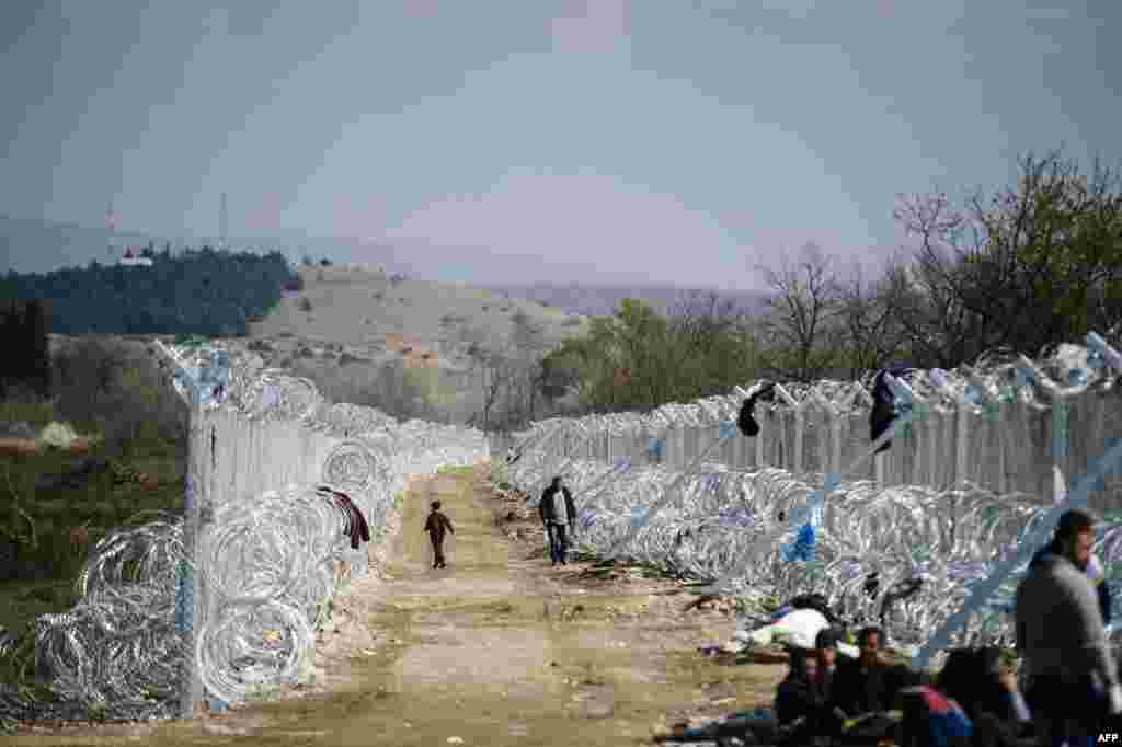 Migrants and refugees walk on a path by a fence and razor wire at the Greek-Macedonian border, near the Macedonian town of Gevgelija. (AFP/Dimitar Diloff)