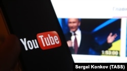 Приложение YouTube в смартфоне на фоне видео с выступлением президента РФ Владимира Путина. Иллюстративное фото