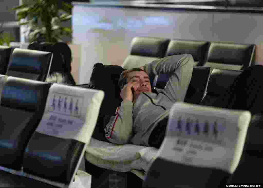 A stranded Russian passenger lies on a bench while calling to his family.