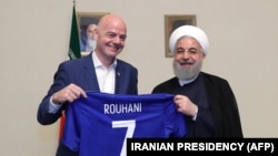 A handout picture released by the office of Iranian President Hassan Rouhani shows him (R) and FIFA President Gianni Infantino holding a football shirt with Rouhani's name during Infantino's visit to the capital Tehran on March 1, 2018.