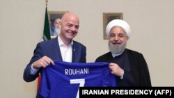 Eron prezidenti Hasan Ruhoniy (o‘ngda) va FIFA prezidenti Janni Infantino Tehronga 2018 yilgi safari chog‘ida Ruhoniyning nomi yozilgan futbolkani ushlab turibdi.